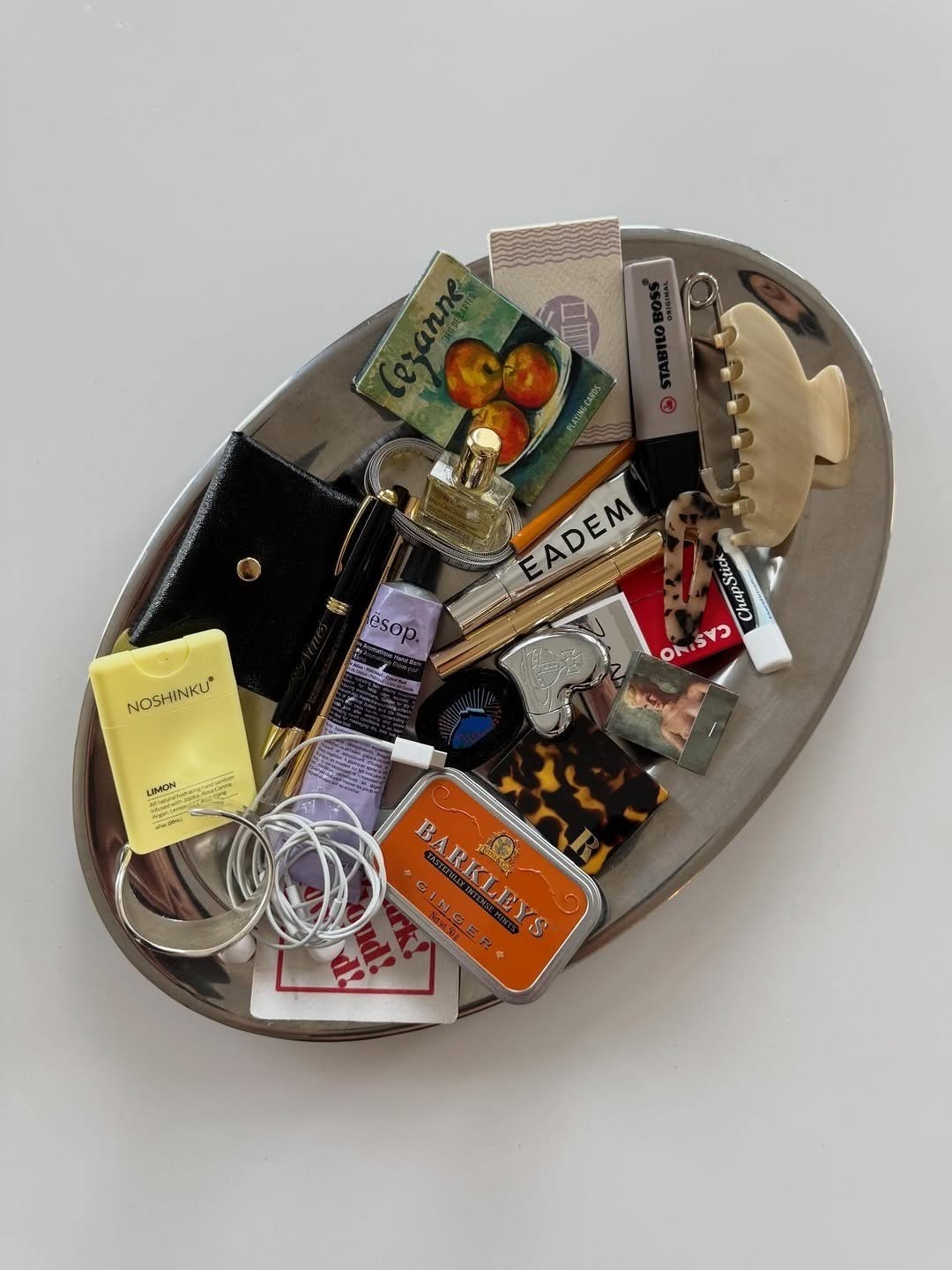 A silver tray filled with everyday objects, from lilac hand balm to a silver heart lighter.
